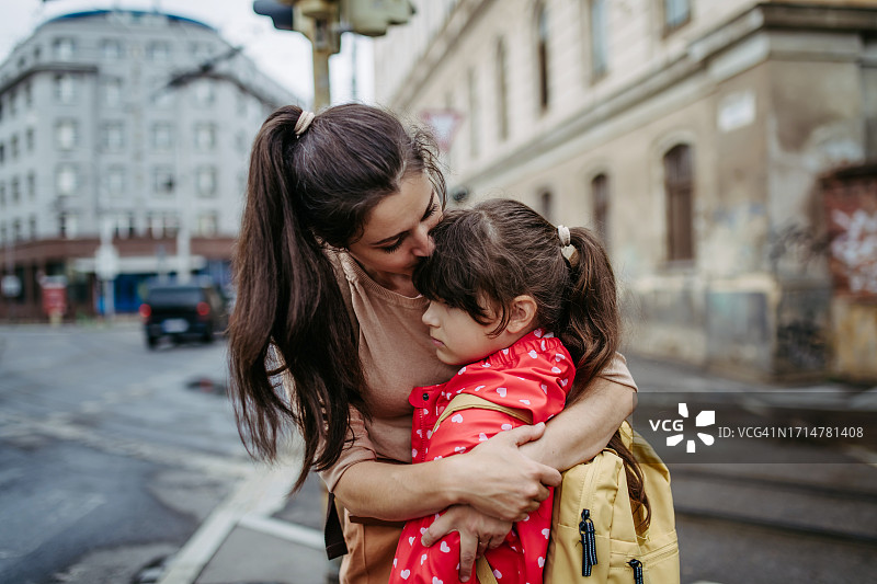 母亲在城市街道上拥抱女儿。焦虑的年轻女孩不想去上学，害怕被欺负图片素材