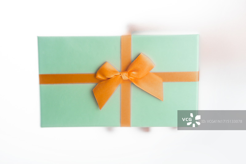 手拿橙色丝带礼品盒特写。图片素材