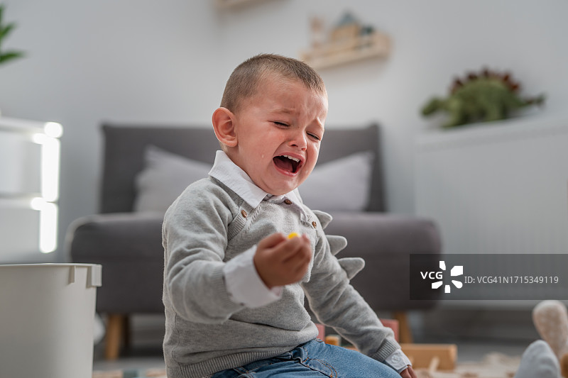 一个幼儿男孩坐在家里地板上哭泣图片素材