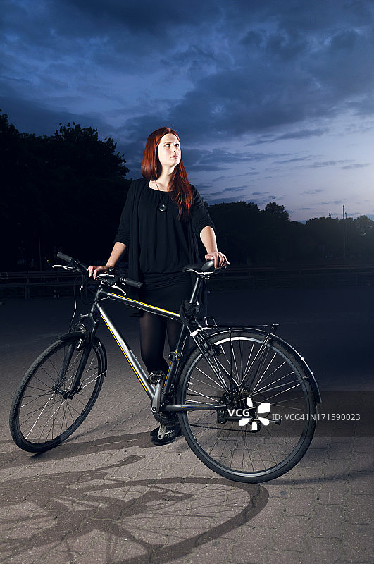 夜晚站在自行车旁的年轻女人图片素材