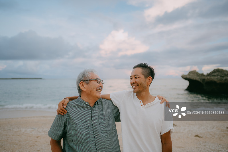快乐的老年父亲和成年的儿子在黄昏的海滩上图片素材