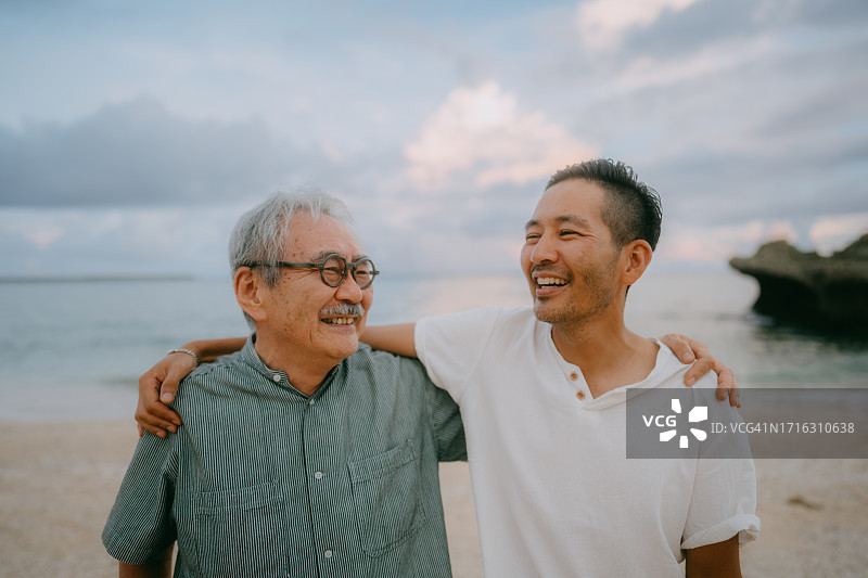 年长的父亲和成年的儿子在黄昏的海滩上图片素材