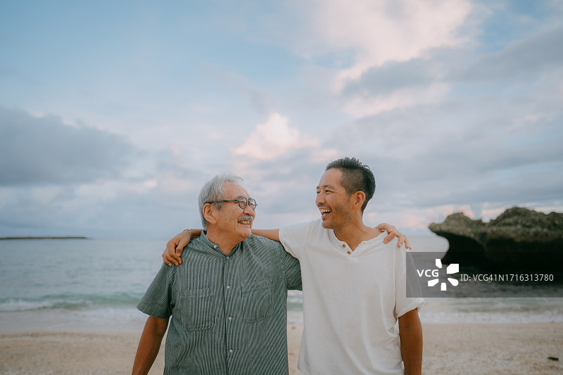 年长的父亲和成年的儿子在黄昏的海滩上图片素材