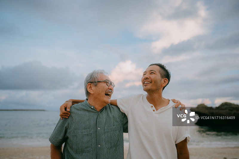 年长的父亲和成年的儿子在黄昏的海滩上图片素材