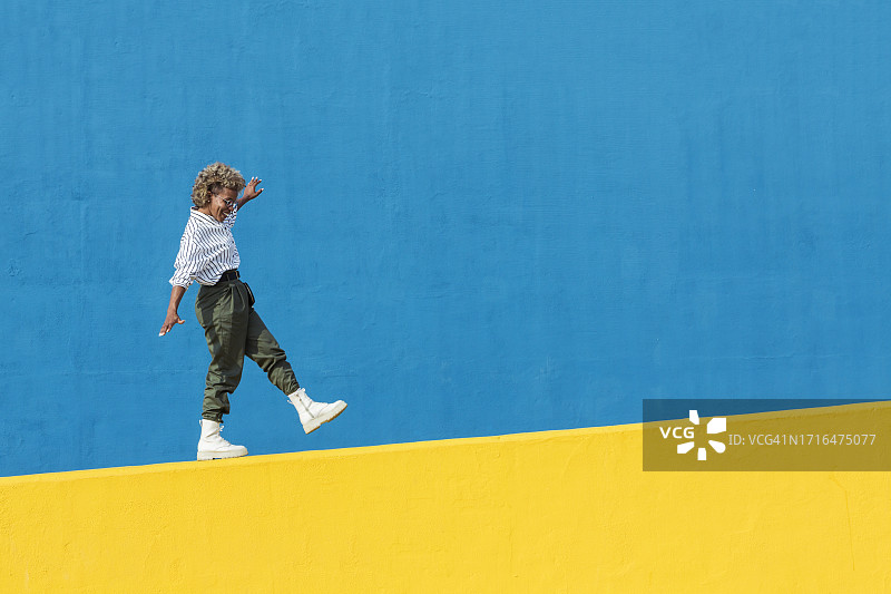 快乐的年轻拉丁美洲女性在黄色墙壁外行走，自由自在的概念图片素材