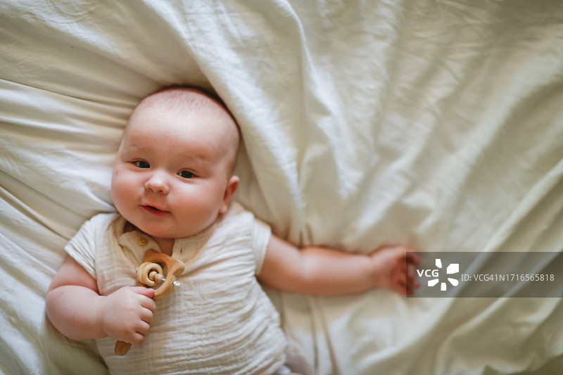 安全又有趣：胖乎乎的四个月大婴儿仰卧，手拿环保玩具摇铃，留白图片素材
