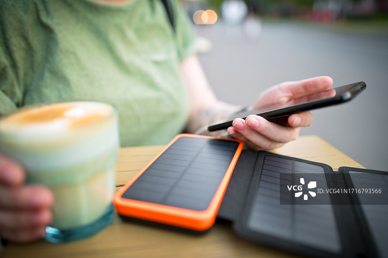在咖啡馆用太阳能电池板为智能手机充电的年轻女人图片素材