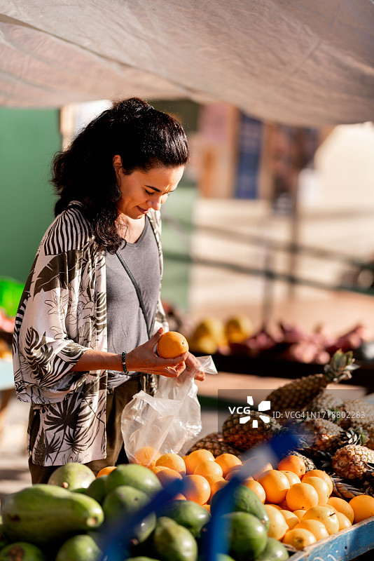 微笑的女人在户外市场摊位上购买橙子和水果图片素材