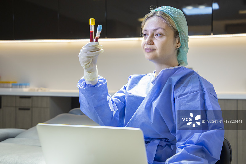 年轻的金发医务人员在诊所里拿着血样试管，并在笔记本电脑上录入信息图片素材