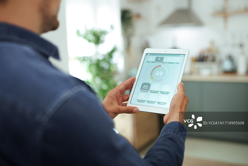 男人在现代客厅使用平板电脑上的智能家居应用程序调节温度图片素材
