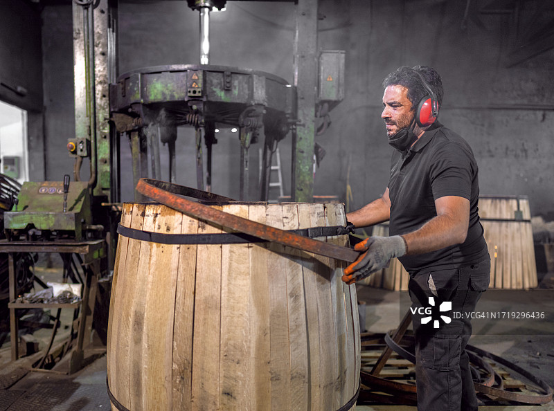 在赫雷斯的桶匠车间里，一名工人将桶放在章鱼机上，该机器将放置金属带，以保持桶板的气密性。雪利酒桶用于盛放葡萄酒和威士忌。图片素材
