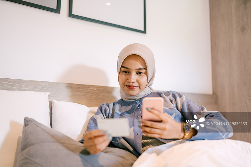 坐在床上使用智能手机的亚洲头巾妇女图片素材