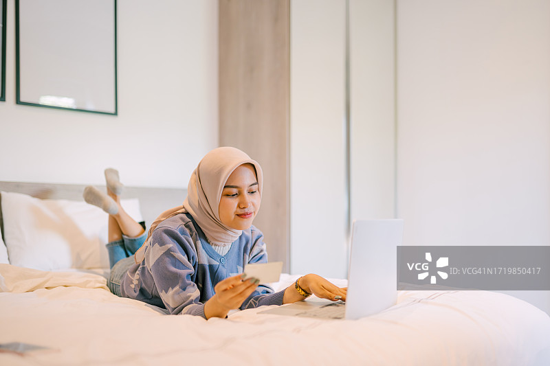 戴头巾的亚洲女人在卧室里用笔记本电脑网购图片素材