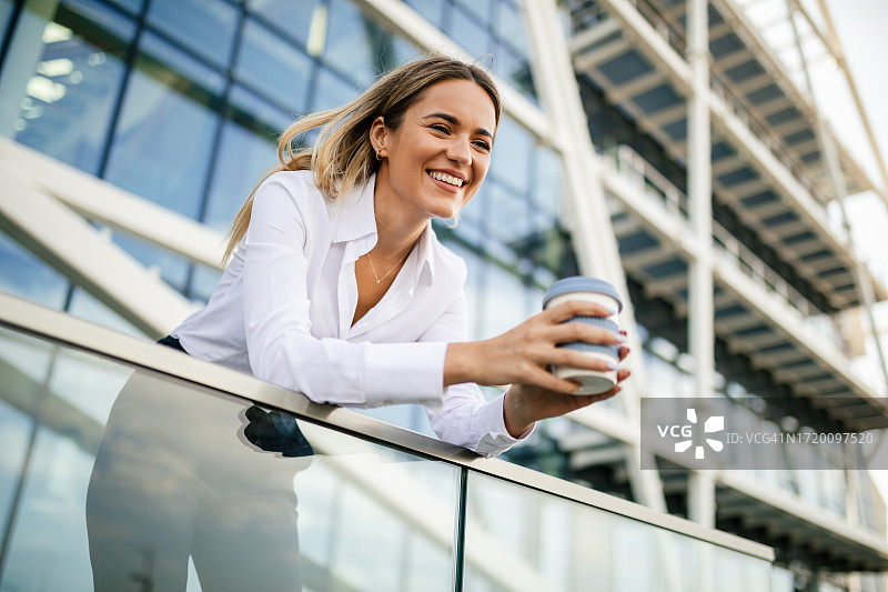 在现代办公楼前享受咖啡休息的户外商务女人图片素材
