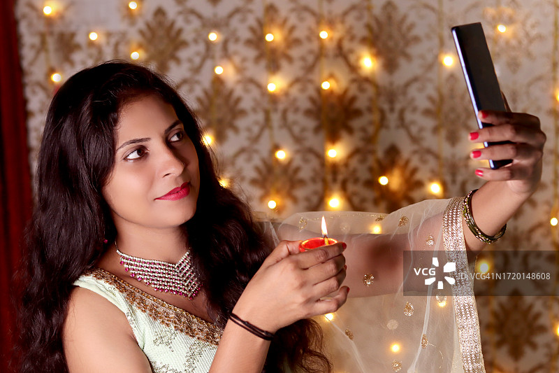 年轻女子用智能手机自拍并手持油灯图片素材