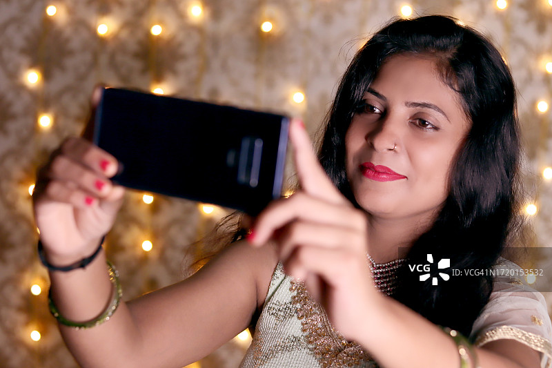 年轻女人在浅色背景下用智能手机自拍图片素材