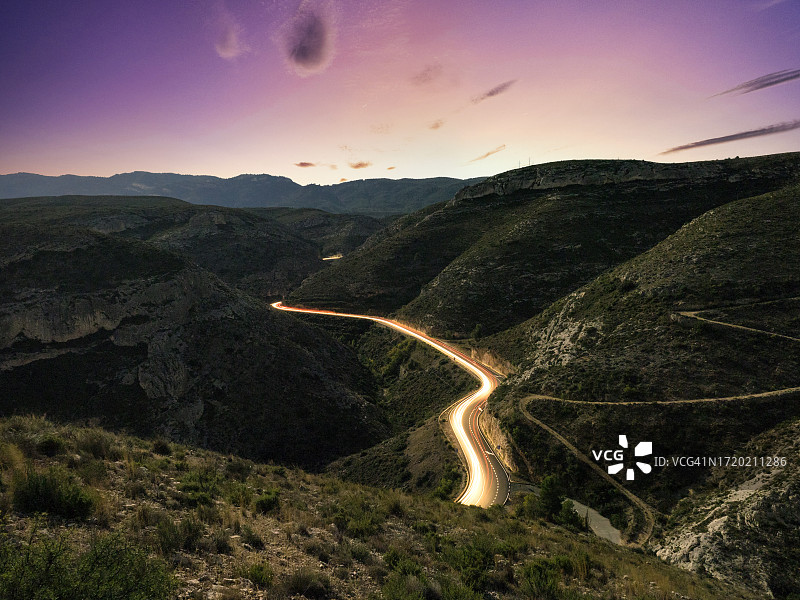 日落时分，弯曲道路上行驶车辆的光轨山景图片素材