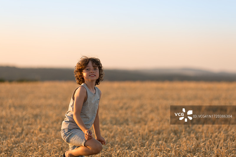 在麦田里玩耍的8岁卷发男孩图片素材