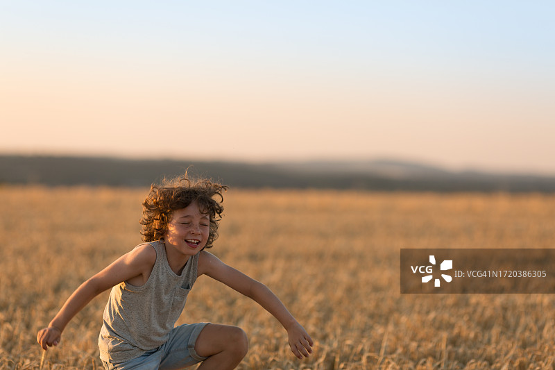 在麦田里玩耍的8岁卷发男孩图片素材