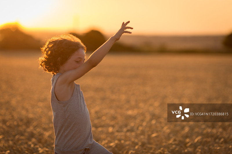 在麦田里跳舞的8岁卷发男孩图片素材