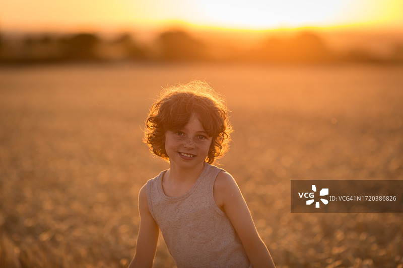 在麦田里微笑的8岁卷发男孩图片素材