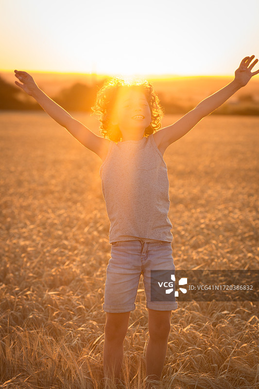 在麦田里欢笑跳跃的8岁卷发男孩图片素材