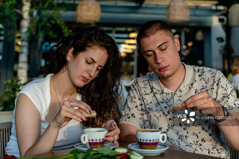 年轻夫妇在咖啡馆花园里往咖啡里加糖图片素材