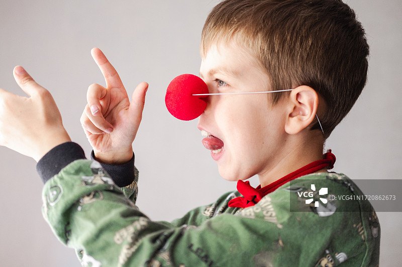 戴着小丑鼻子吐舌头的9岁男孩的肖像：儿童的强烈情感，淘气的男孩图片素材