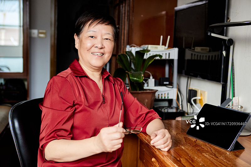 老年妇女坐在卧室的桌旁使用平板电脑图片素材