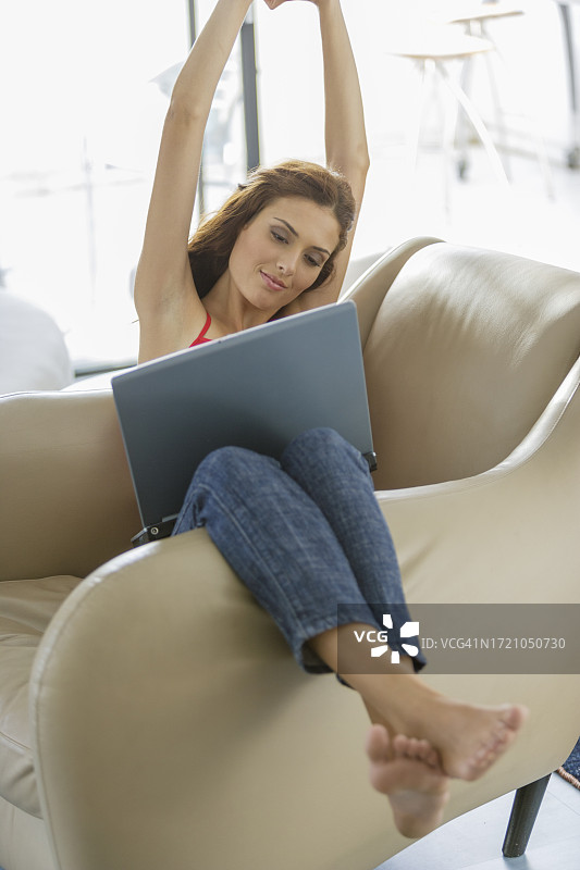 坐在扶手椅上使用笔记本电脑的年轻黑发女子图片素材