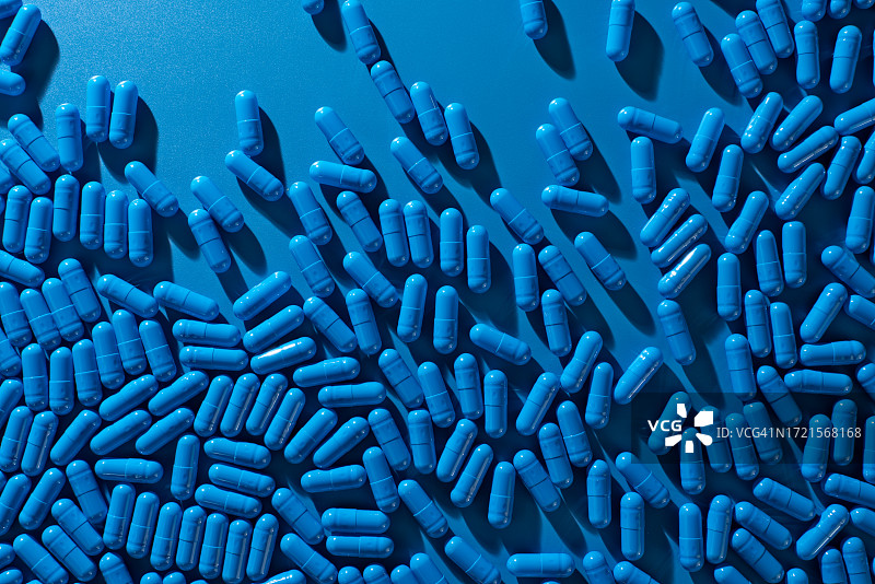 蓝色背景上散落的蓝色胶囊药丸图片素材