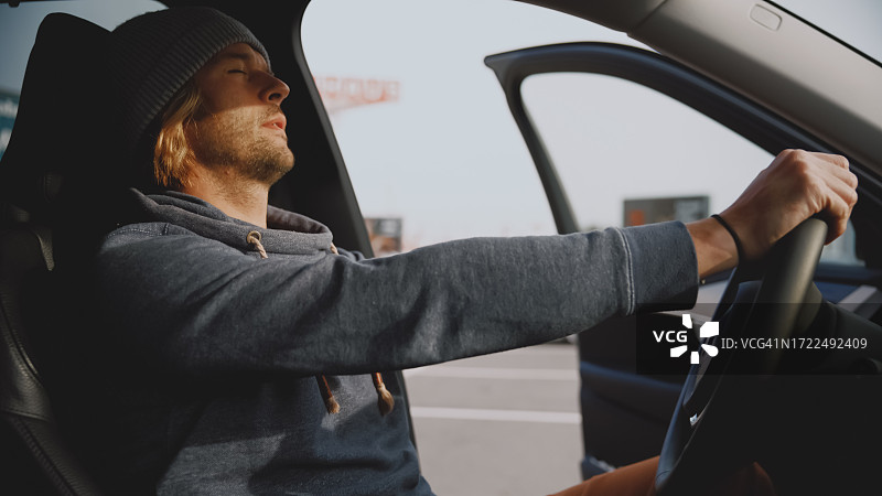 年轻男人在打开车门的汽车内休息，手握方向盘图片素材