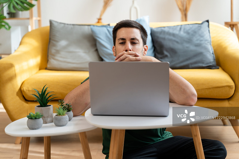 疲惫的年轻人在家穿着休闲服，在使用笔记本电脑时打呵欠图片素材