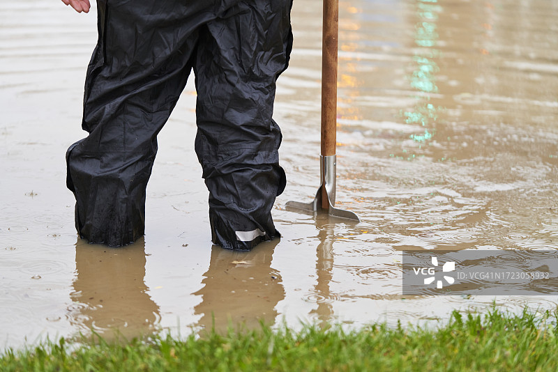 站在被水淹没的街道上，试图用工具疏通下水道的人的背影图片素材