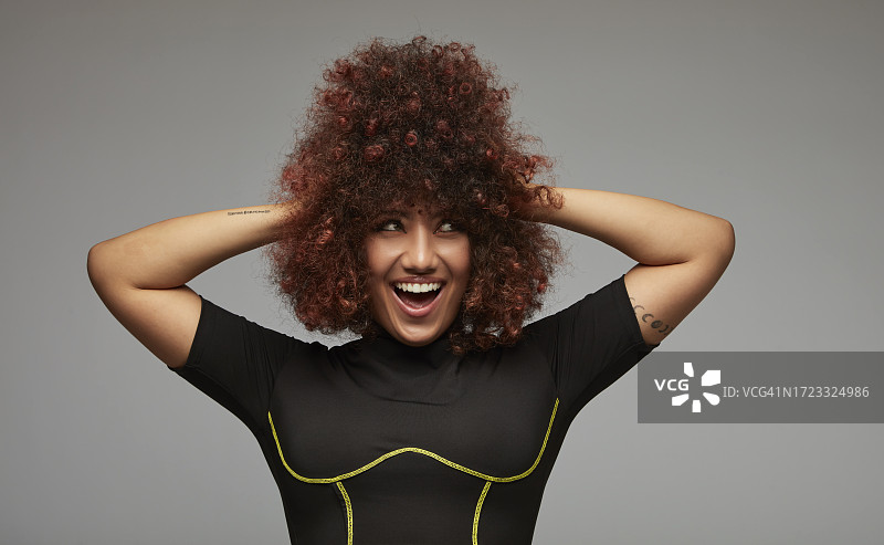 双手放在蓬松卷发上的微笑混血青年女人图片素材