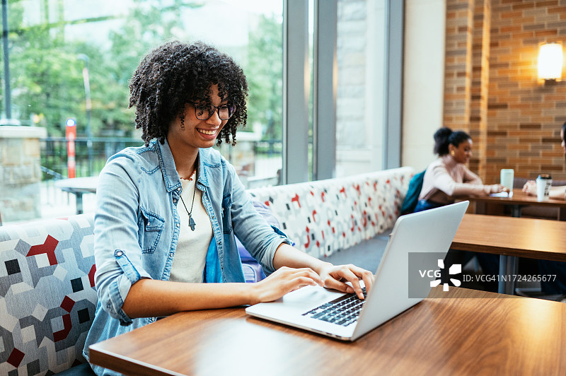 在酒店大堂使用笔记本电脑的卷发混血学生图片素材