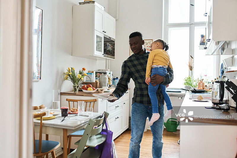 非洲男子抱着儿子，同时在厨房的桌子上放盘子图片素材