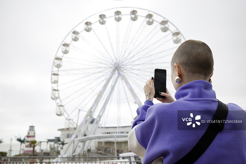 一位年轻女性在海边拍摄摩天轮游乐设施图片素材