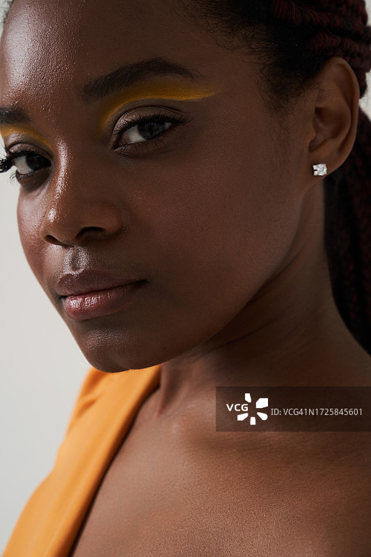 佩戴耳环、化着黄色妆容的非裔美国年轻女人的美丽肖像特写。美容概念，有文案空间。图片素材