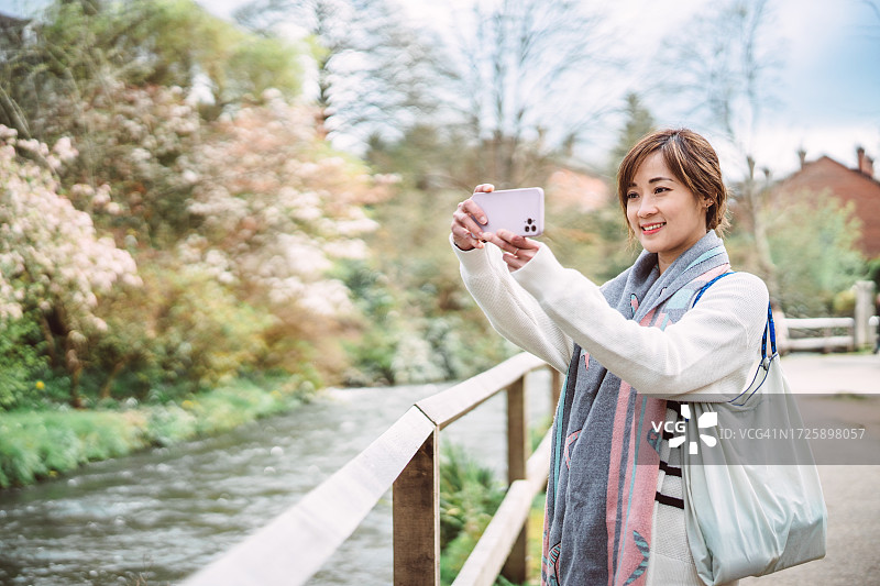 年轻女游客在度假时用智能手机拍摄美丽城镇的自然风光图片素材
