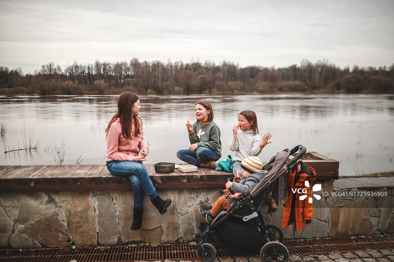 河畔野餐：兄弟姐妹在河边享受健康的野餐，在步行旅行中享用午餐盒里的蔬菜图片素材