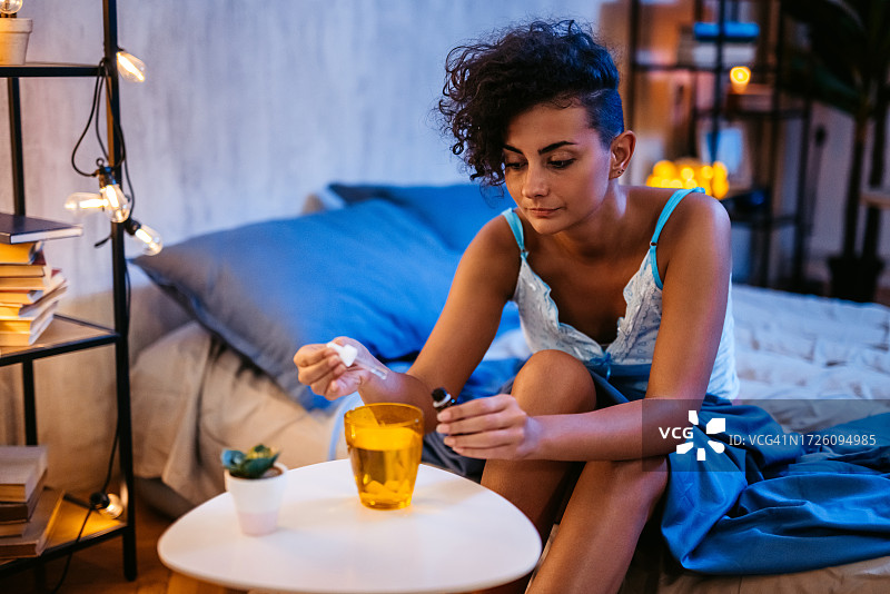 年轻女人睡前在玻璃杯水中滴药图片素材