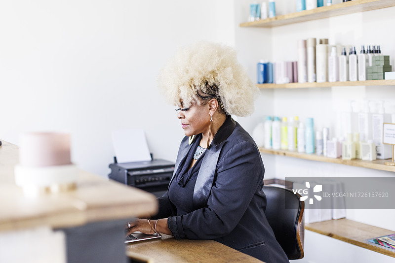 中年女接待员在美发沙龙办公桌前使用笔记本电脑图片素材