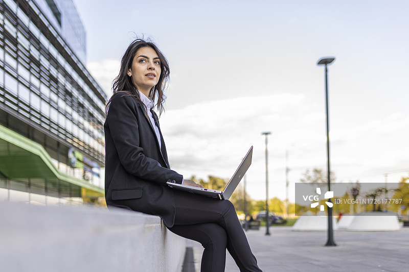 在商业区户外穿着西装，用笔记本电脑在互联网上搜索信息的漂亮女人图片素材