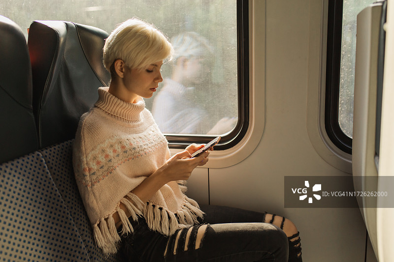 使用手机的金发女人。火车上的乘客图片素材