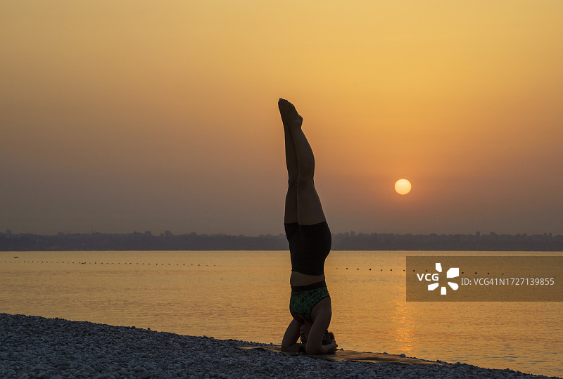 中年美丽女人在日出时于海滩练习瑜伽图片素材