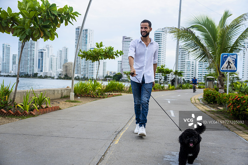 在哥伦比亚卡塔赫纳巴伊亚埃尔拉吉托遛狗的拉丁美洲男子图片素材