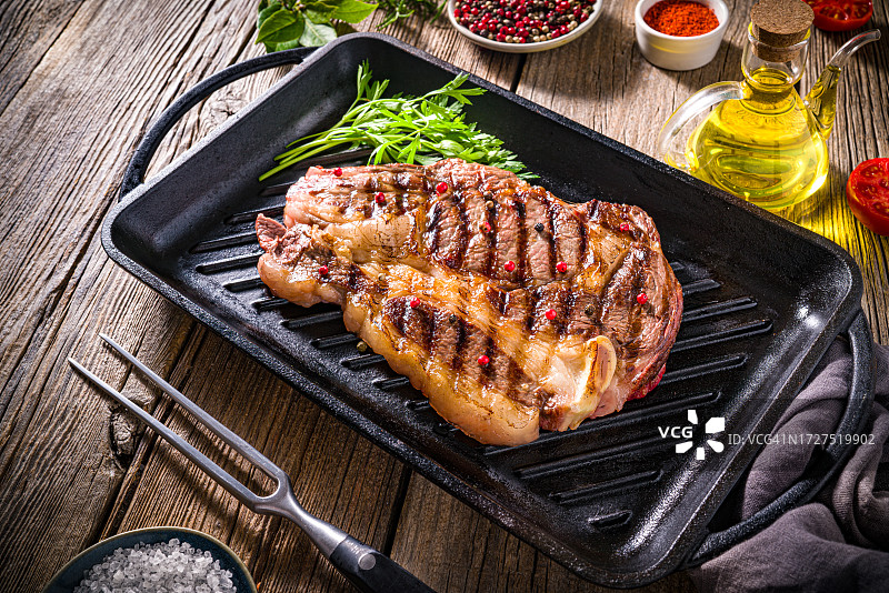 在铸铁烤架上烤制的带香草橄榄油、番茄、辣椒配料的烤牛肋排图片素材