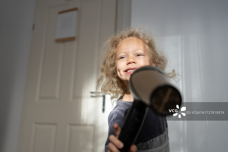 微笑的女孩在家吹干头发，玩得很开心图片素材