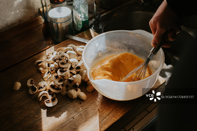 在碗里搅拌鸡蛋的男人特写，碗旁边是蘑菇砧板图片素材